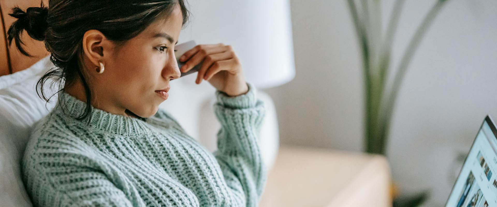 Woman sitting on a cozy couch wearing a chunky sweater looking at her laptop.